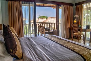 A hotel room with a bed, a desk, and a balcony with a view. - Living Asia Resort Spa Lombok (Senggigi)