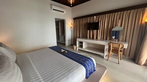 A hotel room with a large bed, a desk with a chair, a television, and a wardrobe. - Living Asia Resort Spa Lombok (Senggigi)