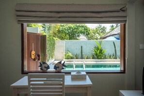 A room with a view of a swimming pool, a wooden door, and a small table with a chair. - Living Asia Resort Spa Lombok (Senggigi)