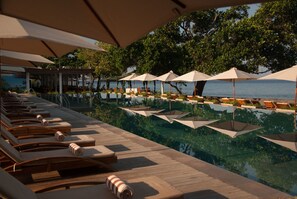 An infinity pool with lounge chairs and umbrellas, surrounded by trees and a view of the sea. - Living Asia Resort Spa Lombok (Senggigi)