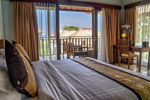 A hotel room with a bed, a table, chairs, and a view of the sea through large windows. - Living Asia Resort Spa Lombok (Senggigi)