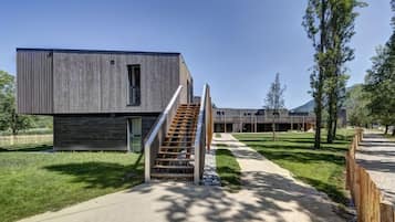 A modern building with a wooden exterior, a staircase leading to a door, and a pathway with trees.