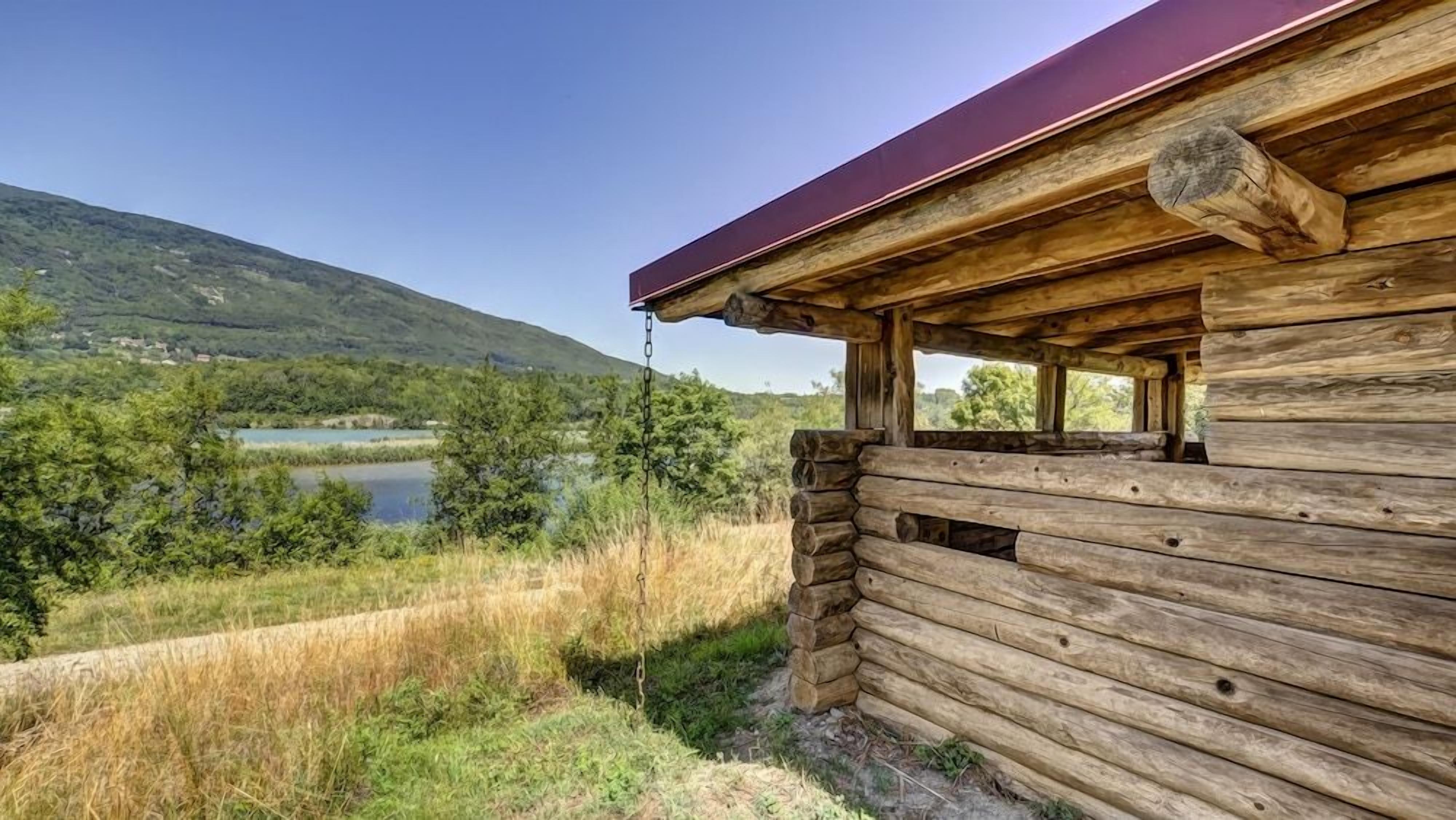 A wooden cabin with a view of a lake and hills.