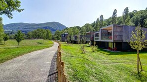 A modern building with a curved driveway, surrounded by greenery and hills.