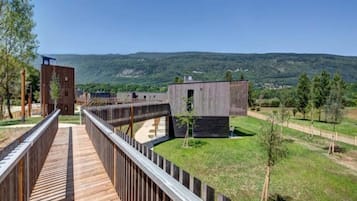 A wooden deck leading to a modern building with a view of a hilly landscape.
