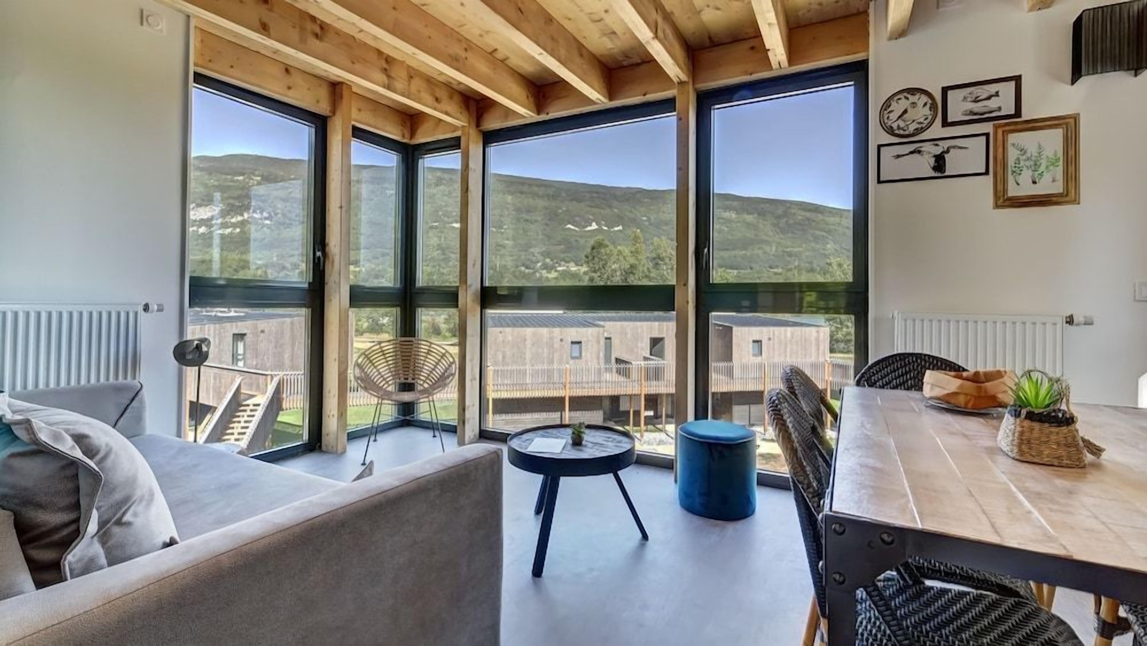 Interior moderno com amplas janelas, área de refeições e vista para uma paisagem montanhosa.