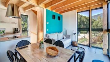 A modern interior with a wooden dining table, a sofa, and a view of the outdoors.