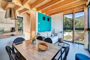 A modern interior with a wooden dining table, a sofa, and a view of the outdoors. - Le Village des Oiseaux (Motz)