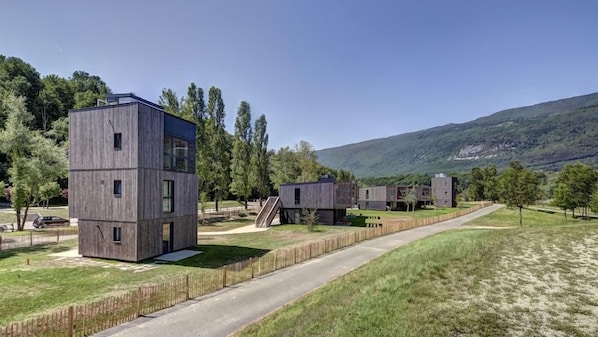 A modern building complex with a central tower, connected structures, and a surrounding grassy area. - Le Village des Oiseaux (Motz)