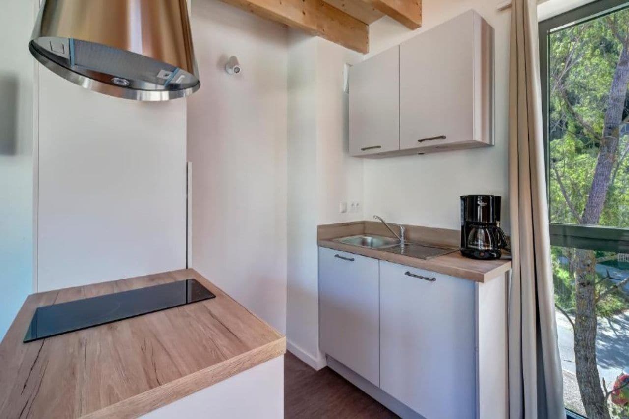 A compact kitchen with a stainless steel range hood, a wooden countertop, a sink, and cabinets.