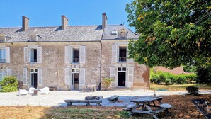 A two-story stone building with shuttered windows, a gravel courtyard, and outdoor seating. - A wing of a charming 18th-century château, fully renovated and set in a magnificent park (Saint-Étienne-de-Montluc)