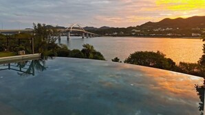 Une vue d’un pont enjambant une étendue d’eau au coucher du soleil, avec une piscine au premier plan.