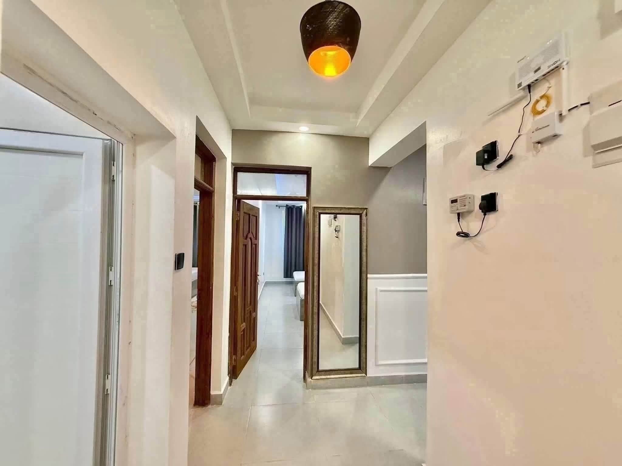 Un pasillo con paredes blancas, una lámpara en el techo y una puerta que da a otra habitación.