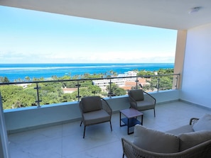A balcony with two wicker chairs, a small table, and a view of the ocean and cityscape. - Nyali Luxury Apartments  (Mombasa)
