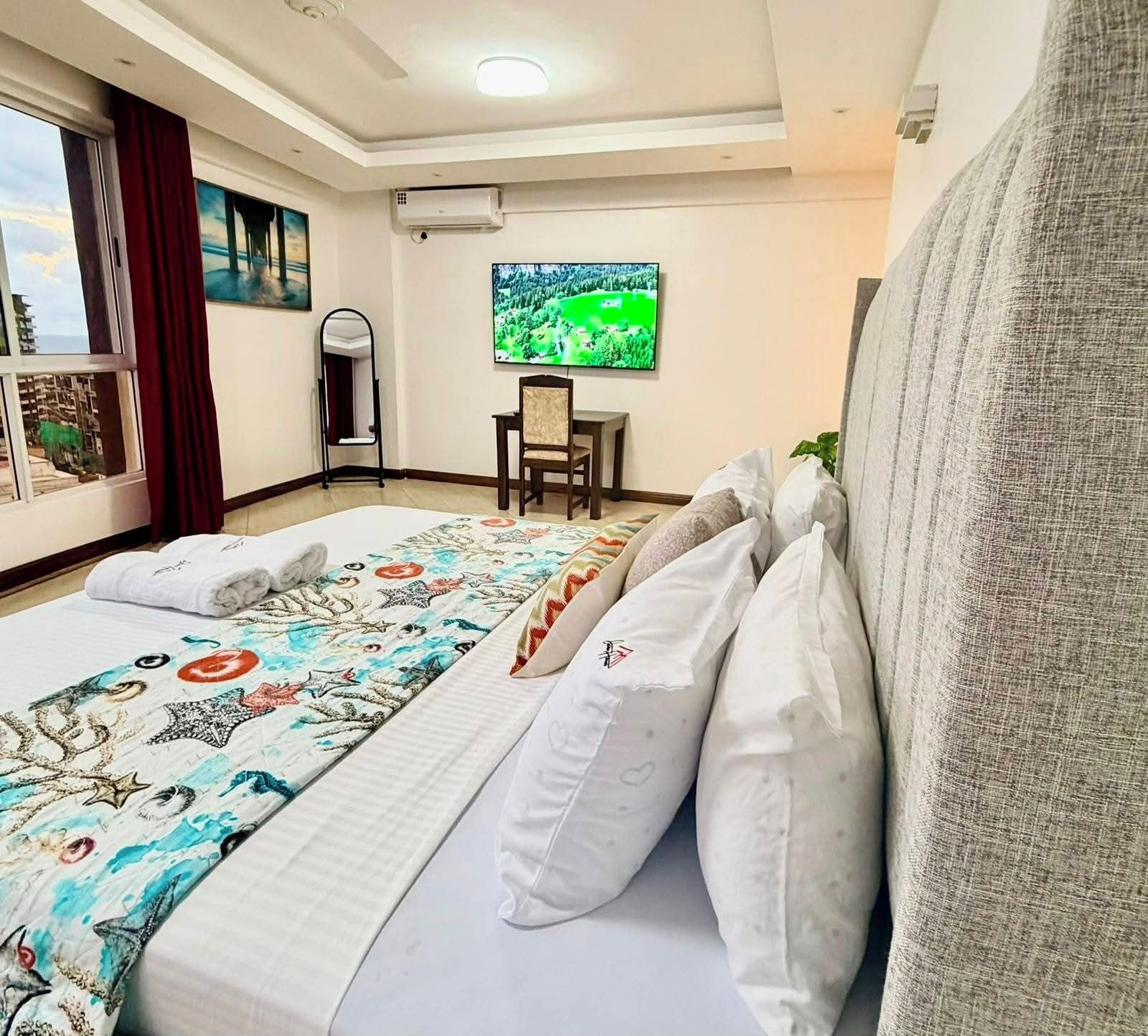 Habitación de hotel con cama, televisor, sillón y vista al exterior.
