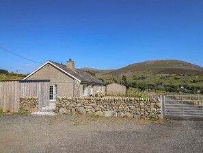 A stone house with a wooden fence and a metal gate, set against a backdrop of hills and a clear sky. - Tyn Y Weirglodd (Caernarfon)