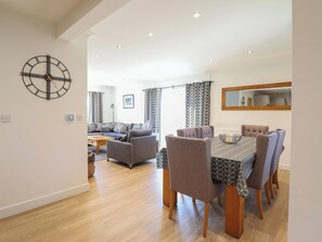 A spacious living area with a dining table and chairs, a sofa, and a large wall clock. - Tyn Y Weirglodd (Caernarfon)