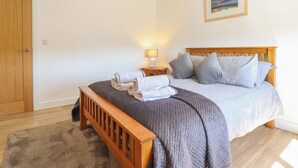 A bedroom with a wooden bed, grey bedding, a nightstand with a lamp, and a painting on the wall. - Tyn Y Weirglodd (Caernarfon)