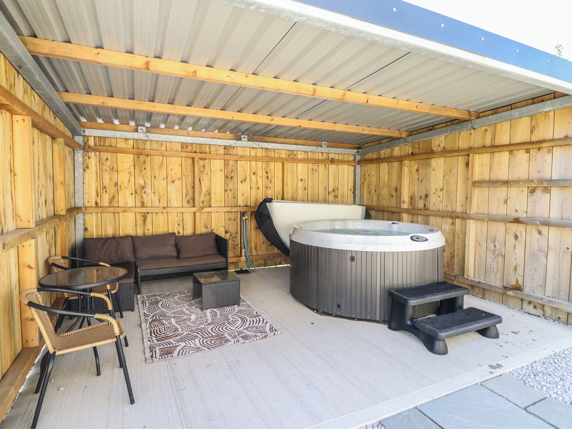 A covered outdoor area with a hot tub, a sofa, and two chairs.