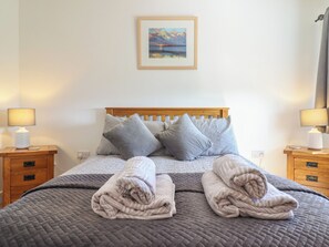 Ein ordentlich bezogenes Bett mit einer gesteppten Decke, zwei Kissen und zwei gefalteten Handtüchern. Über dem Bett hängt ein Gemälde.