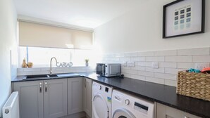 A compact kitchen with a sink, a Bosch washing machine, a Bosch microwave, and a framed picture on the wall. - Tyn Y Weirglodd (Caernarfon)