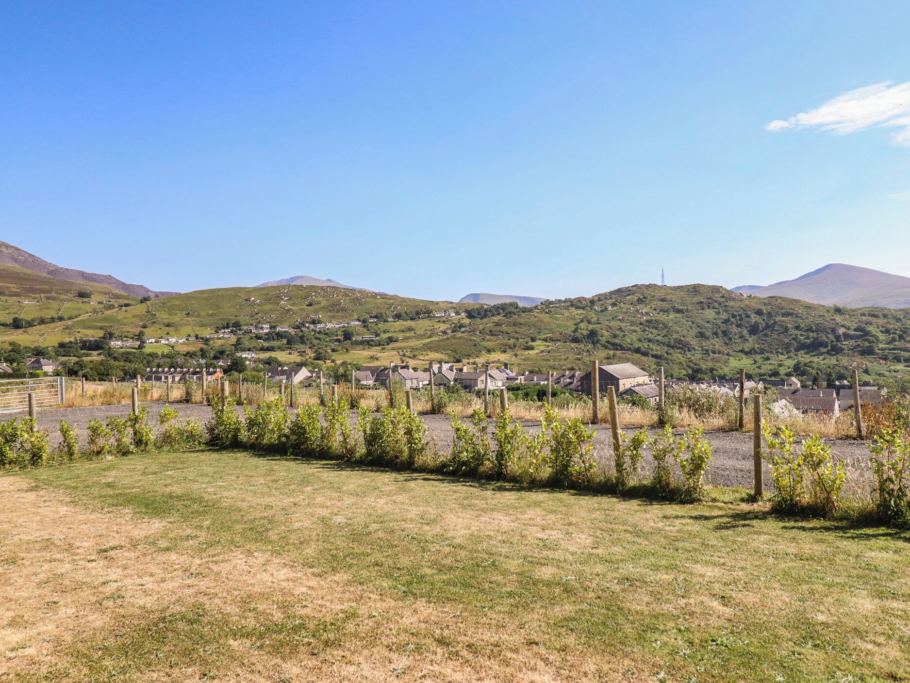 Paesaggio rurale con case, una recinzione e colline sullo sfondo.