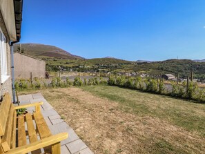 Eine Terrasse mit einer hölzernen Bank und einer Steinmauer, mit Blick auf eine ländliche Gegend mit Häusern und Hügeln.