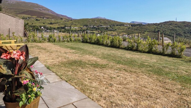 A grassy yard with a stone pathway leading to a building, surrounded by hills and a clear sky. - Tyn Y Weirglodd (Caernarfon)
