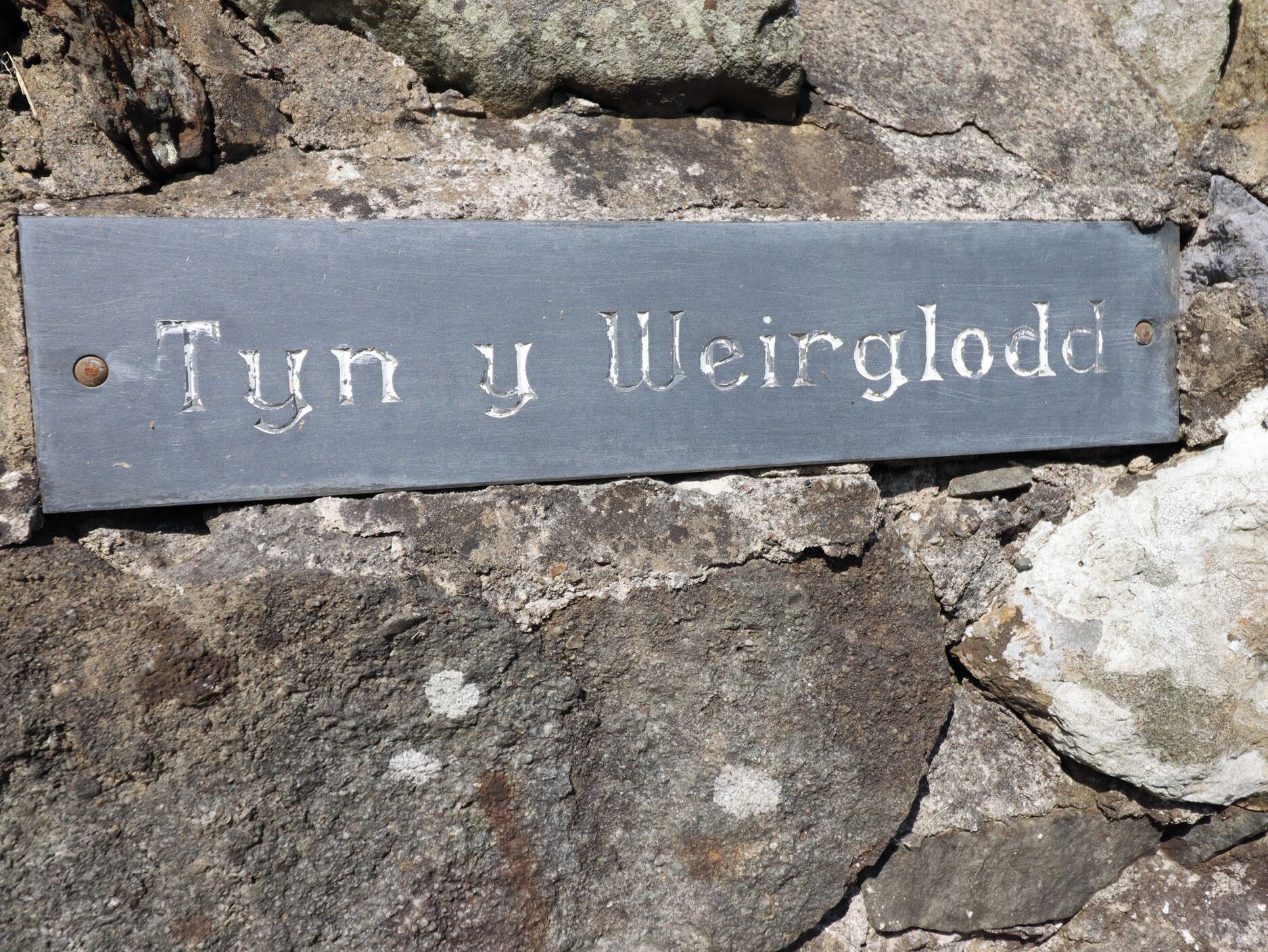 A slate sign with the inscription 'Tyn y Weirgloedd' mounted on a stone wall.