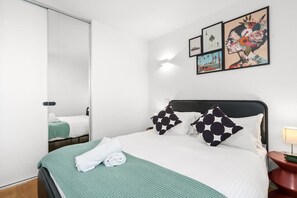 A hotel room with a bed, a nightstand, a lamp, and artwork on the wall. - Walk to Melbourne Uni | Foosball & Free Parking (North Melbourne)