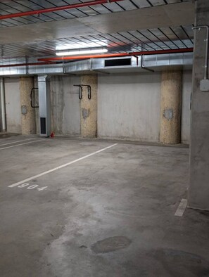 Eine Tiefgarage mit Betonstützen, einem Feuerlöscher und einer Lüftungsanlage.