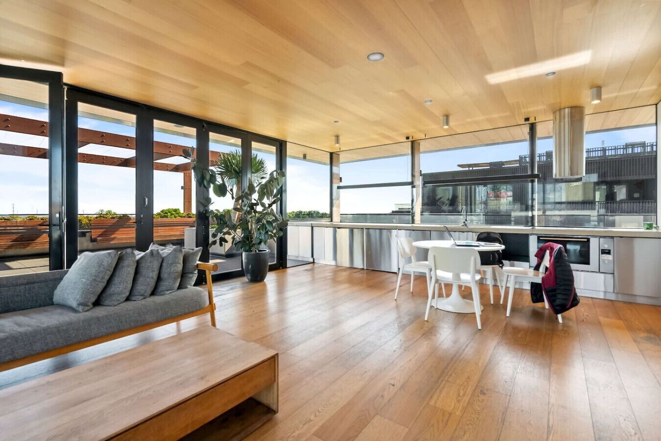 Een modern interieur met houten vloer, een bank, een eettafel met stoelen en een groot raam met uitzicht op de stad.