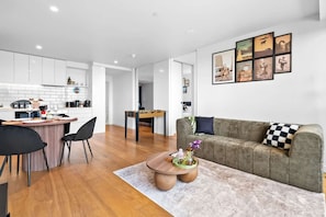 A modern living space with a kitchen, dining area, and a sofa with a checkered pillow. - Walk to Melbourne Uni | Foosball & Free Parking (North Melbourne)