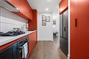 Eine moderne Küche mit roten Schränken, einem Edelstahlkühlschrank und Holzboden.