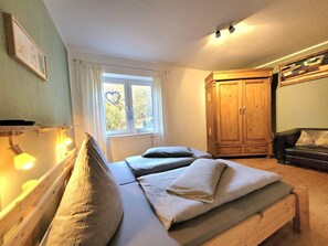 Ein Schlafzimmer mit zwei Betten, einem Holzschrank, einem Fenster mit Herzdeko und Blick auf Bäume.