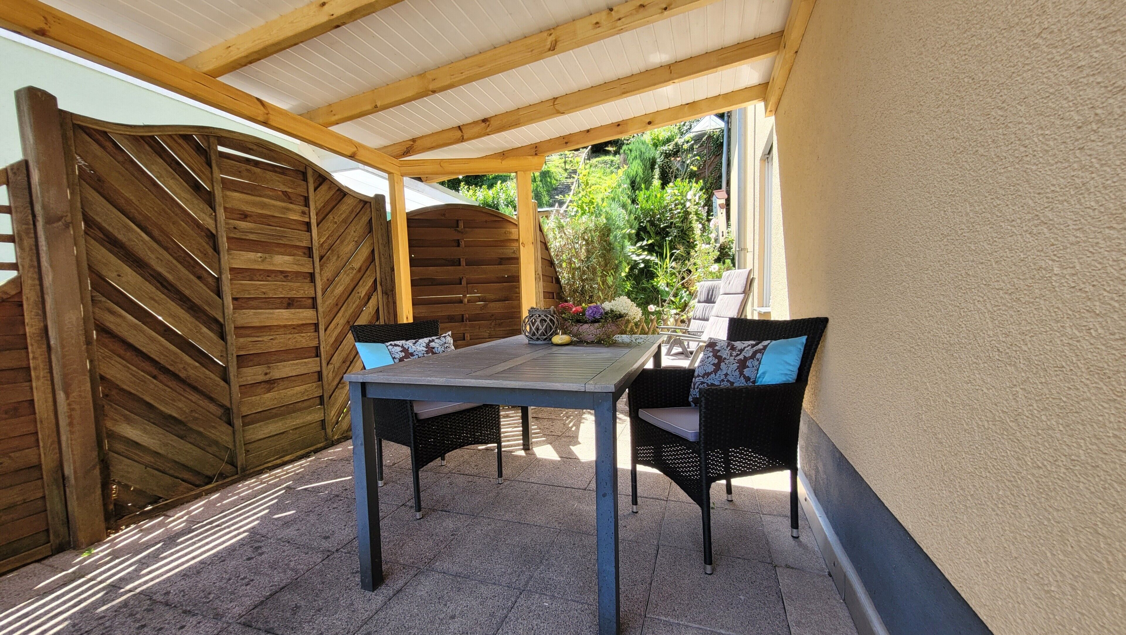 Un patio exterior con una mesa y sillas, un cerco de madera y una zona cubierta.