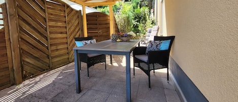 Eine Terrasse im Freien mit Tisch und Stühlen, einem Holzzaun und einem überdachten Bereich.