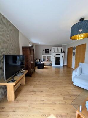 Ein stilvolles Wohnzimmer mit Flachbildfernseher, Holzboden, einem weißen Sofa und einem Kamin.