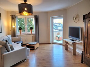 Ein Wohnzimmer mit Sofa, Couchtisch, Fernseher auf einem Schrank, Lampe und einem fenster mit Vorhängen.