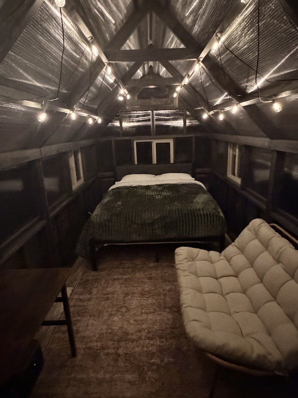 A small, dimly lit attic bedroom with a single bed, a cushioned chair, and a table.