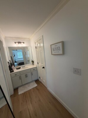 A bathroom with a white vanity, a mirror, and a framed quote on the wall.