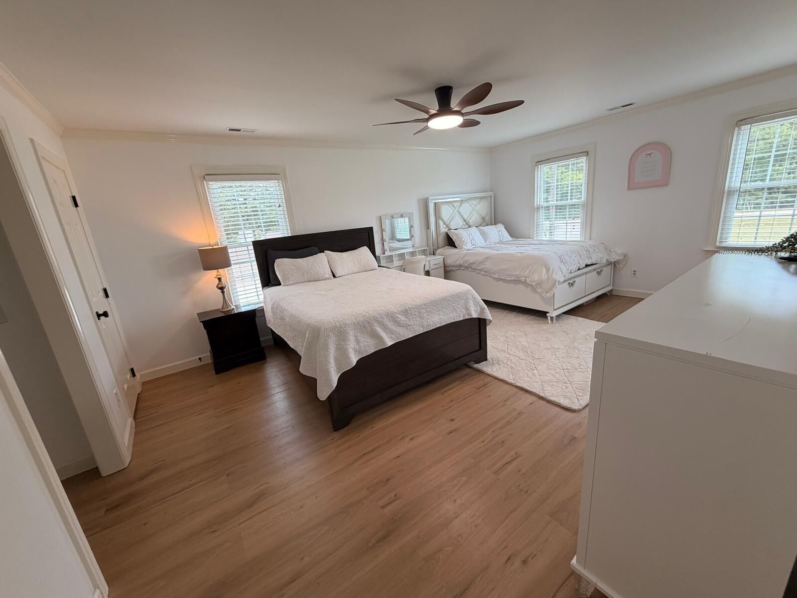 A bedroom with two beds, a ceiling fan, and a large window.