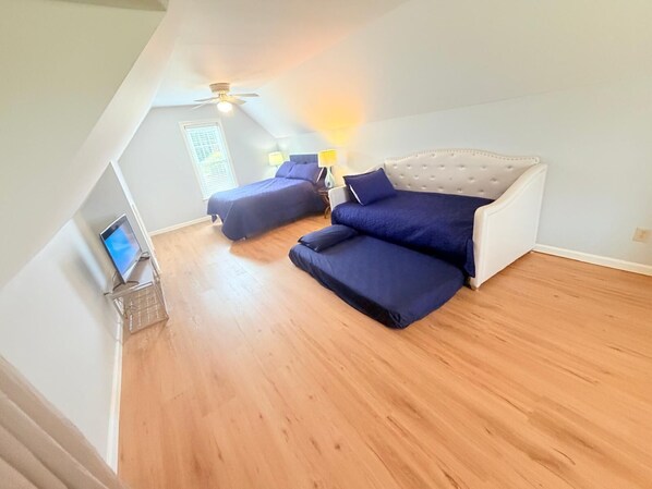A bedroom with a sloped ceiling, two beds, a ceiling fan, and a TV on a stand.