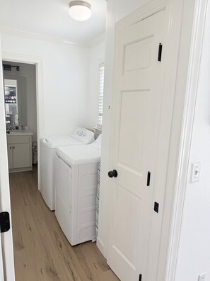 A laundry room with a washing machine and dryer, a door with a black handle, and a wooden floor.