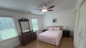 Un dormitorio con cama, cómoda, mesitas de noche, ventilador de techo y ventana.