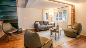 Una sala de estar moderna con un sofá, dos sillones, una mesa de centro y una escalera.