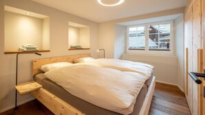Un dormitorio con una cama de madera, una mesita de noche, un espejo y una ventana con vistas a un edificio.