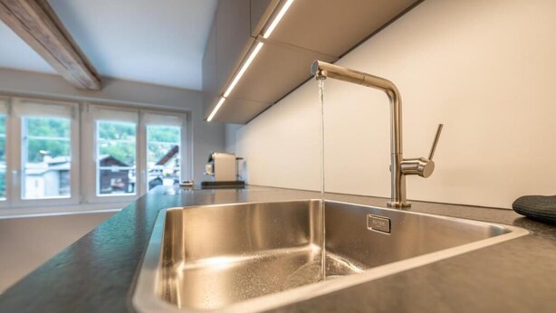 Una cocina moderna con un lavamanos y grifo de acero inoxidable, una ventana con vistas a casas y una encimera.