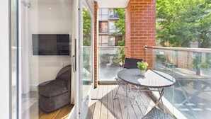 A balcony with a glass door, a small round table with a potted plant, and a chair. - Westminster Residences by apt. (London)