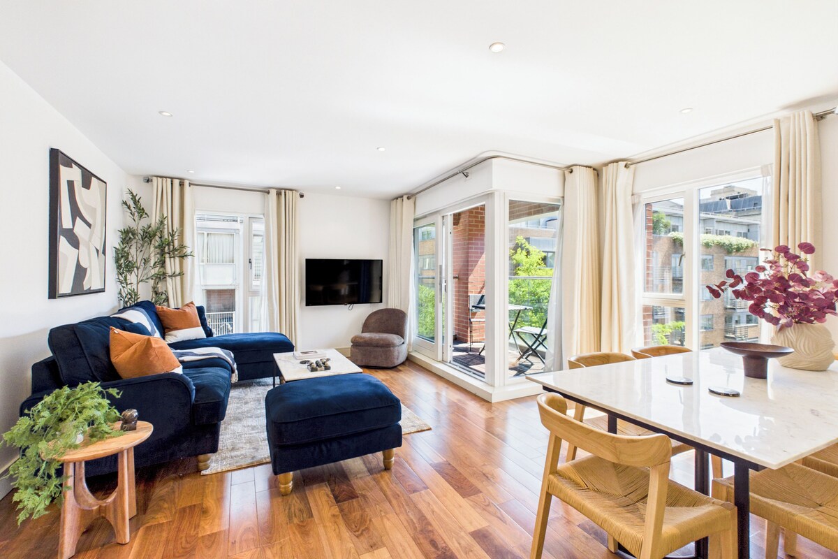 Uma sala moderna com um sofá, um banquinho e uma mesa de jantar com cadeiras.